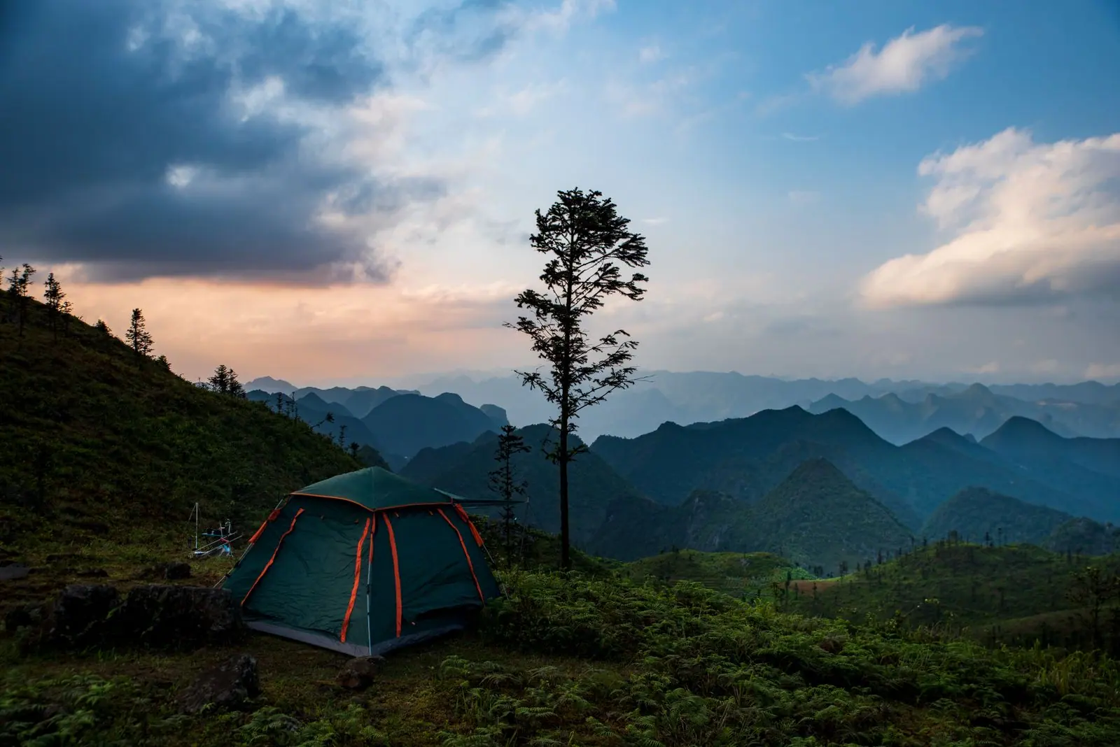 A tent pitched on a grassy hillside with mountains behind it at sunset.