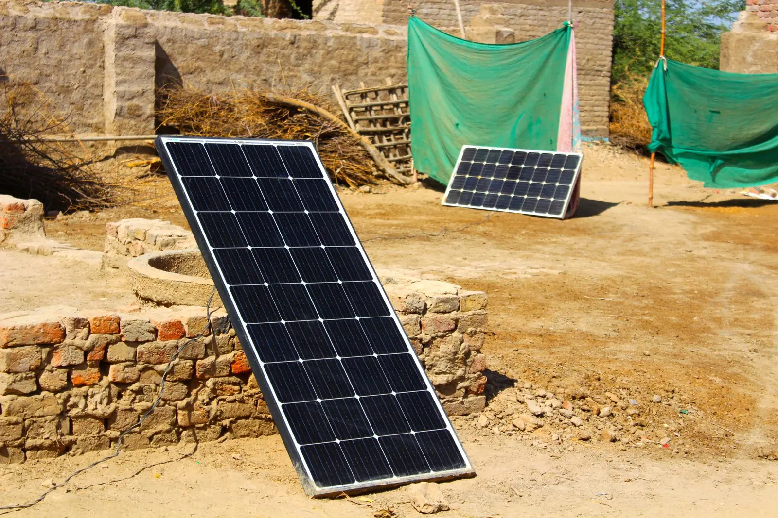 Two portable solar panels set on rocky ground beside low trees.