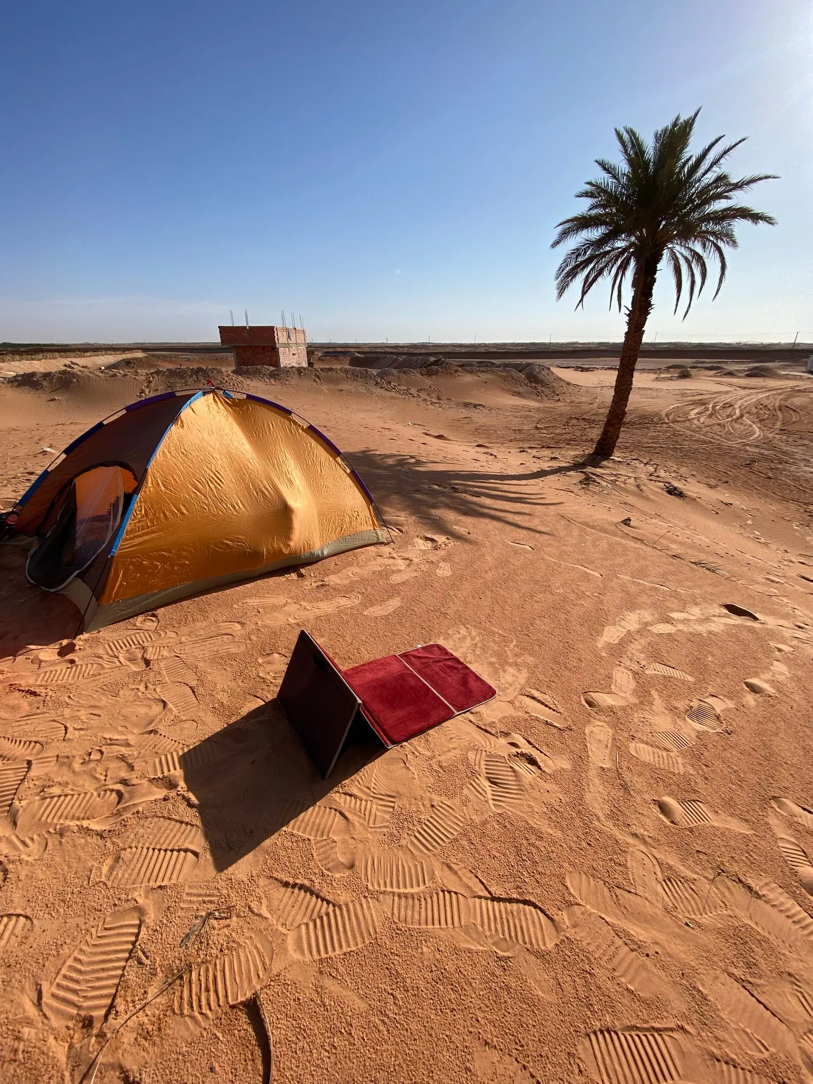 Dome tent on desert sand with a foldable solar panel set up in front.